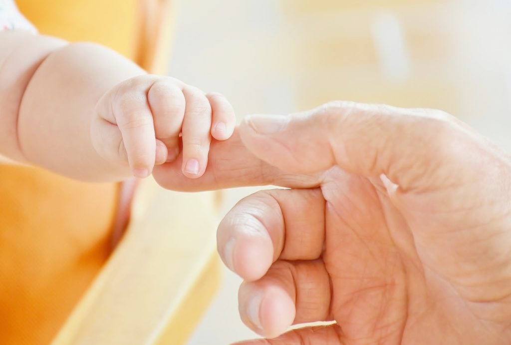 Eine freundliche ältere Person hält die Hand eines Babys.