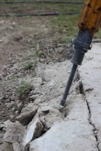 Eine Person bohrt mit einer Bohrmaschine in den Boden.